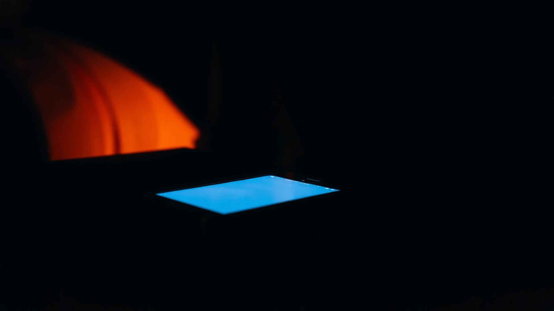 A phone lying face down on a dark bedside table glowing faintly from a notification in cinematic blue and amber light