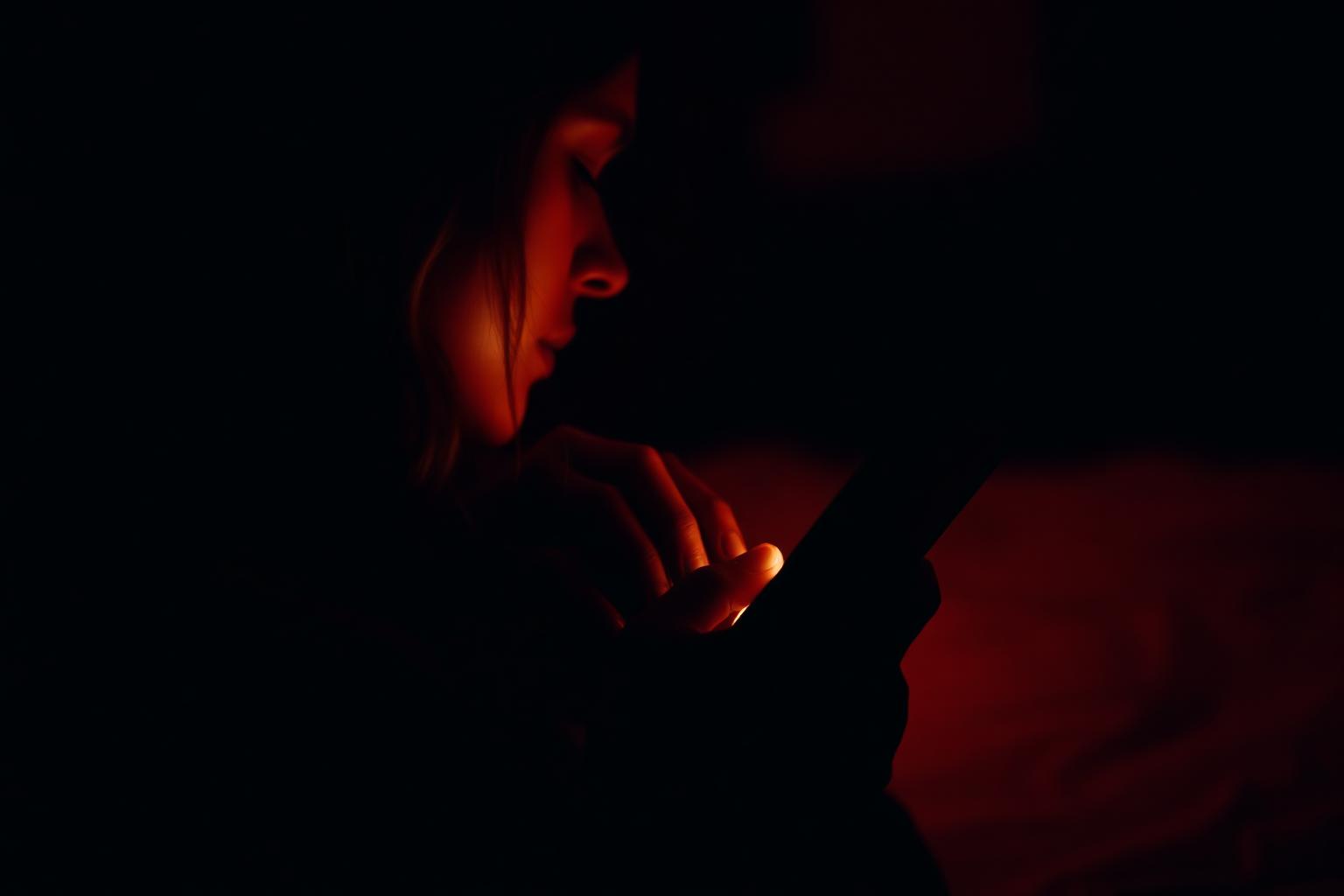 Silhouette of a person in dim red light looking at a glowing phone at night